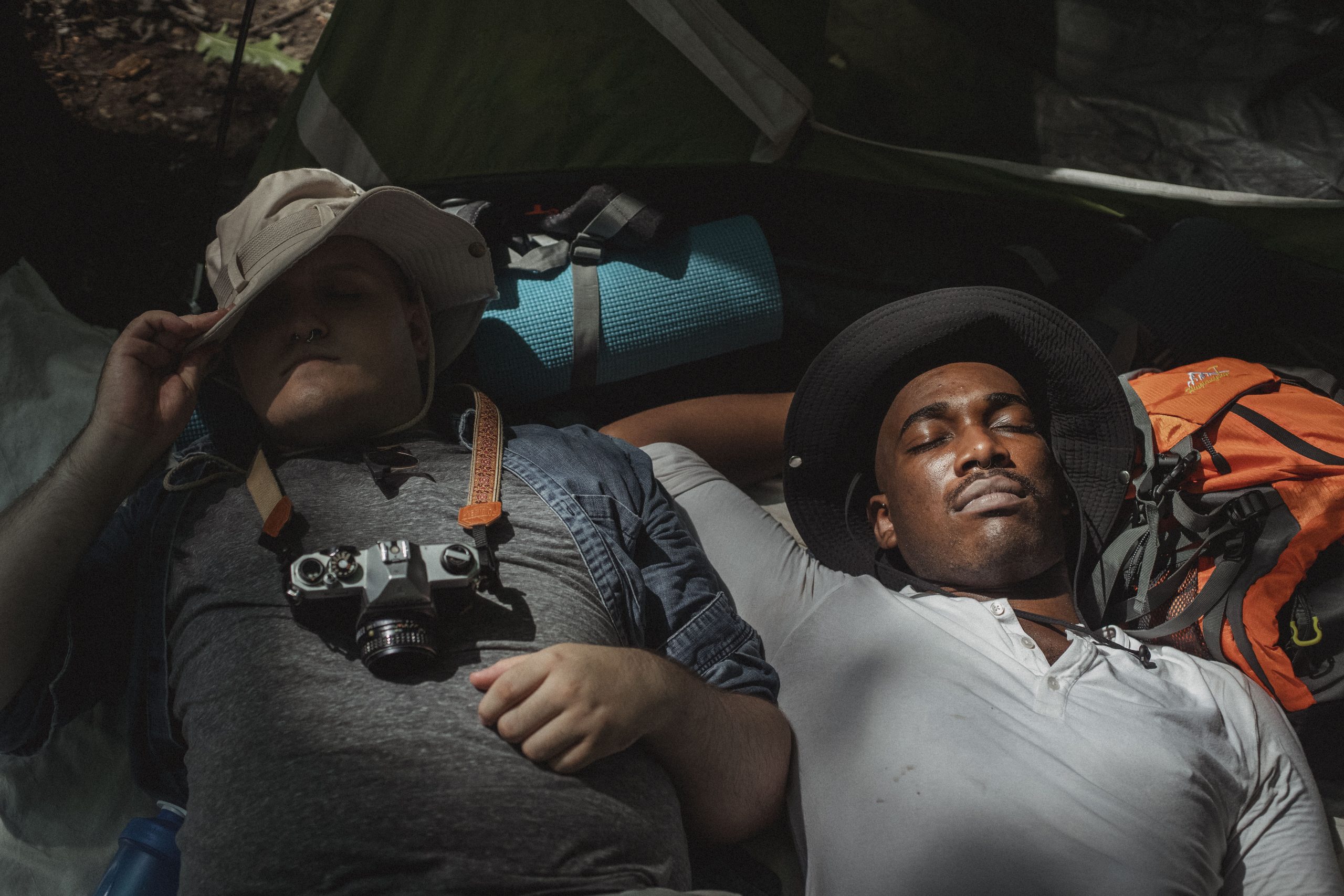 Multiethnic male backpackers napping on rucksacks in soft sunlight