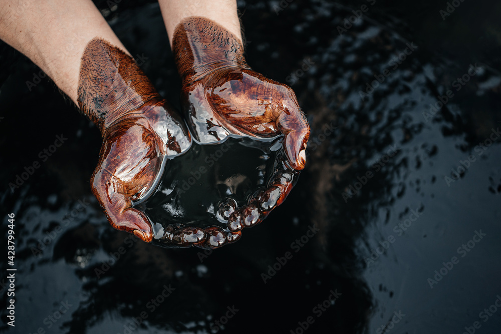 Hands are soaked in crude oil <a href='https://blazenewz.com/category/sport' target='_blank'>against</a> the background of spilled petroleum products. The crisis of the oil industry. Economic downturn. Black gold. Copy space